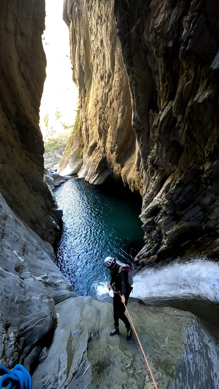 Un participant à une descente canyoning descend en rappel une cascade avec une piscine naturelle magnifique